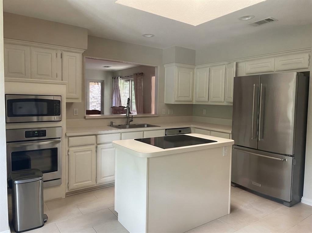 Kitchen featuring a central island with a glass cooktop, stainless steel appliances, recessed ceiling lighting, light-toned cabinetry, and tile flooring