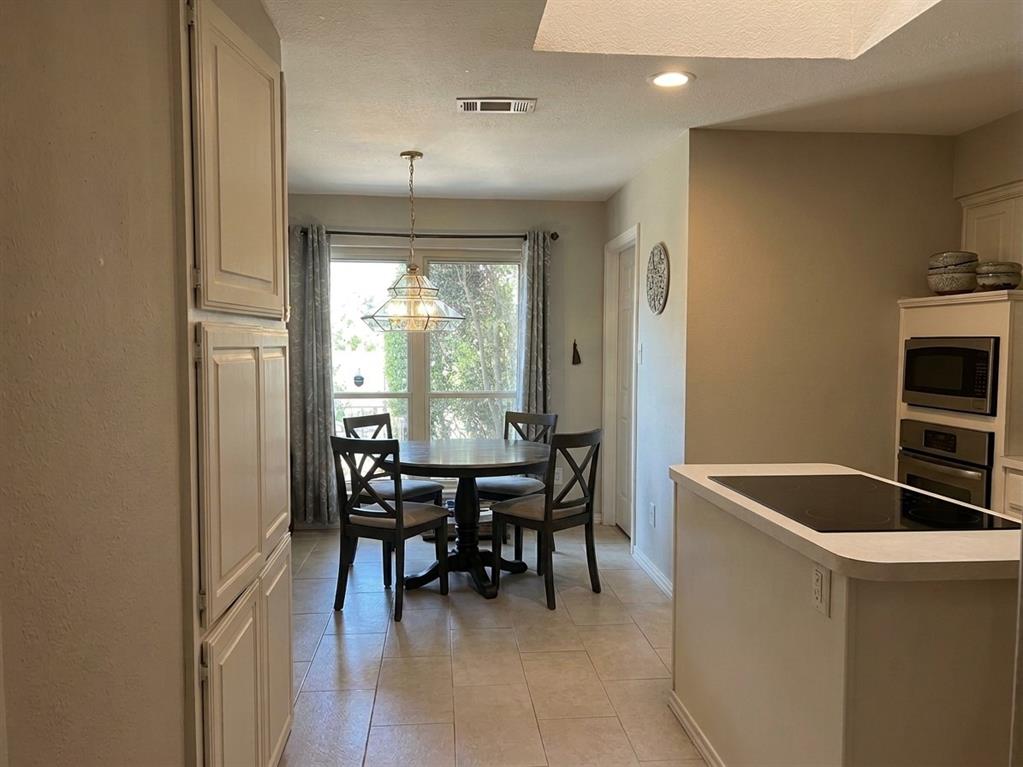 Kitchen featuring tile flooring, built-in wall oven, inset microwave, island with integrated cooktop, and floor-to-ceiling cabinetry