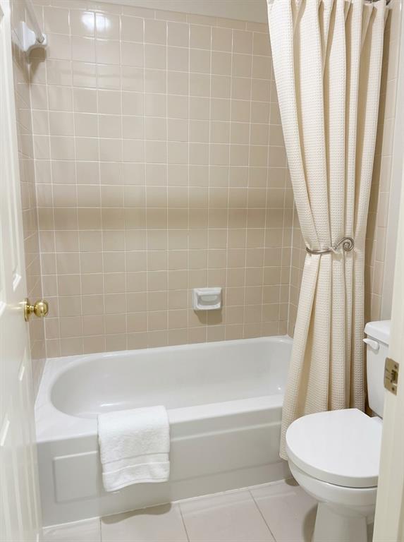 Bathtub with a white acrylic surround, integrated soap dish, ceramic wall tile, and porcelain toilet