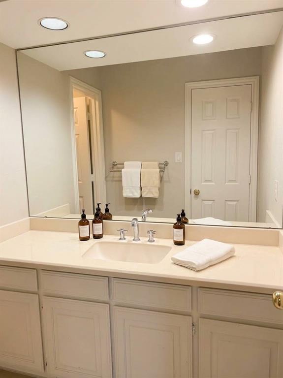 Vanity featuring a solid-surface countertop, integrated rectangular sink, chrome widespread faucet, and recessed-panel cabinetry with a large wall-mounted mirror