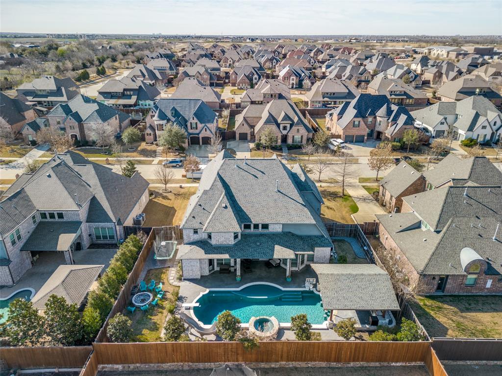 Aerial view of the back of property with the pool, the slide, the diving board, the spa, the tanning bed, the in-pool barstools, and the pergola with the outdoor kitchen.