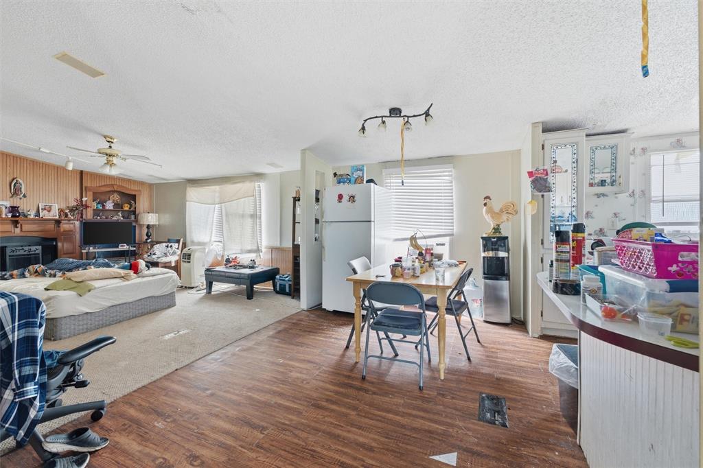Open-concept floor plan featuring wood-finish flooring, built-in fireplace mantle, ceiling fan, and white cabinetry with glass-panel inserts