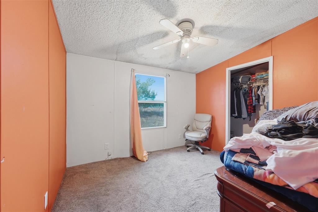 Textured ceiling with a central multi-blade ceiling fan, wall-to-wall carpeting, single-hung window, and a built-in reach-in closet