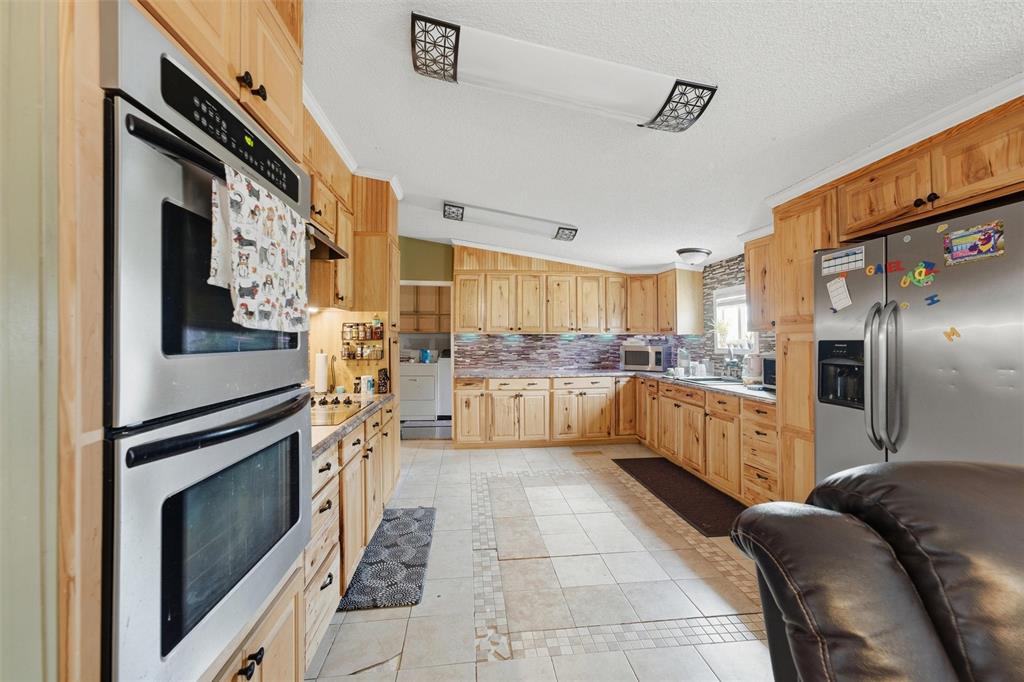 Kitchen featuring natural finish wood cabinetry, stainless steel double wall oven, stone-patterned backsplash, and ceramic tile flooring Kitchen featuring natural finish wood cabinetry, stainless steel double wall oven, stone-patterned backsplash, and ceramic tile flooring