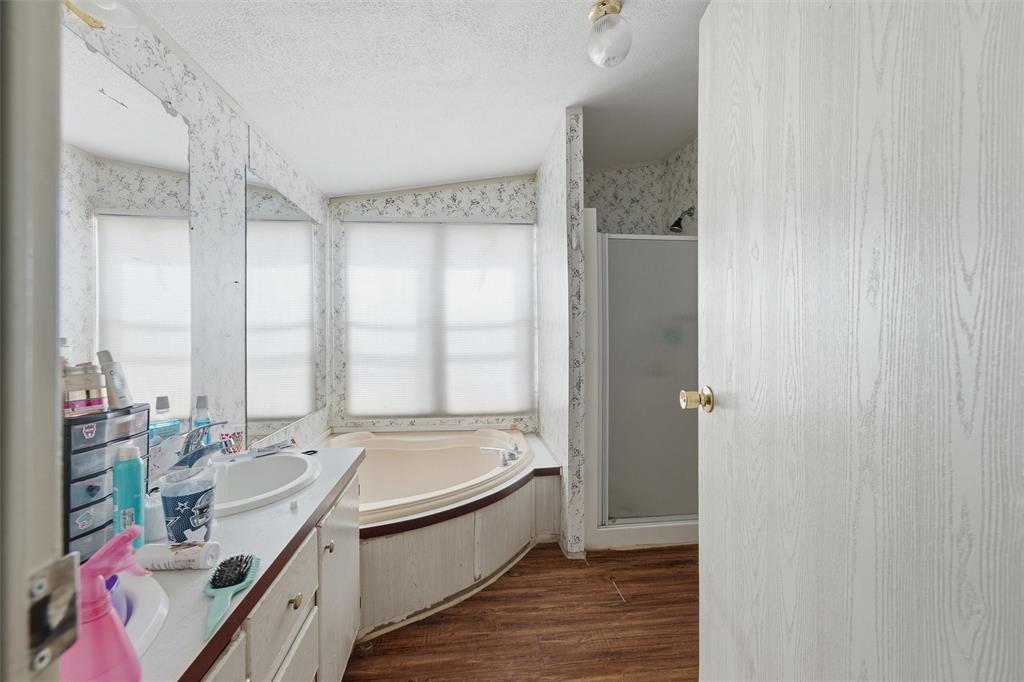 Bathroom featuring a corner soaking tub with a surrounding deck, a wood-finish floor, a wall-to-wall vanity mirror, and a standalone shower stall