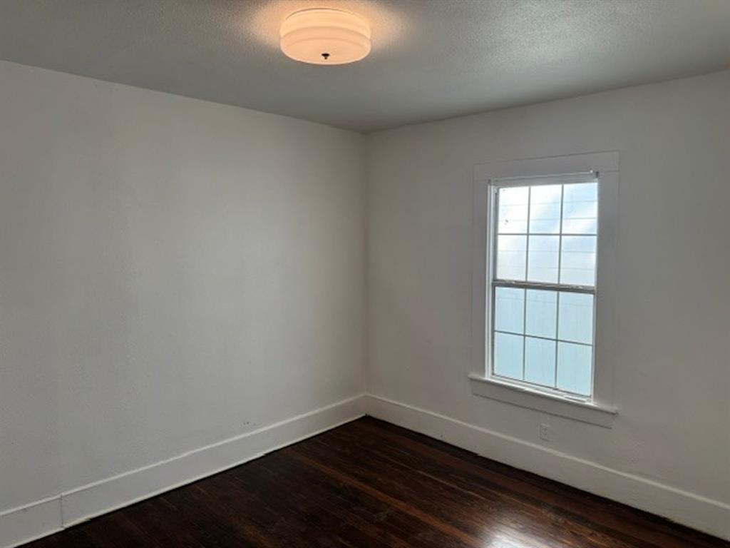White walls with dark wood-finish flooring, featuring a single-pane window with white trim and a flush-mount ceiling light