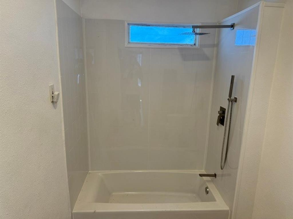 Bathtub with white surround, rainfall showerhead, handheld shower, and horizontal window