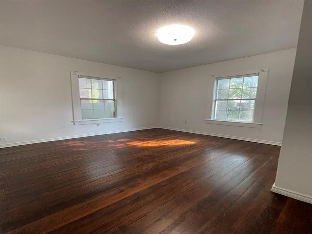 Expansive room featuring dark wood-finish flooring, two large windows, and a flush mount ceiling light