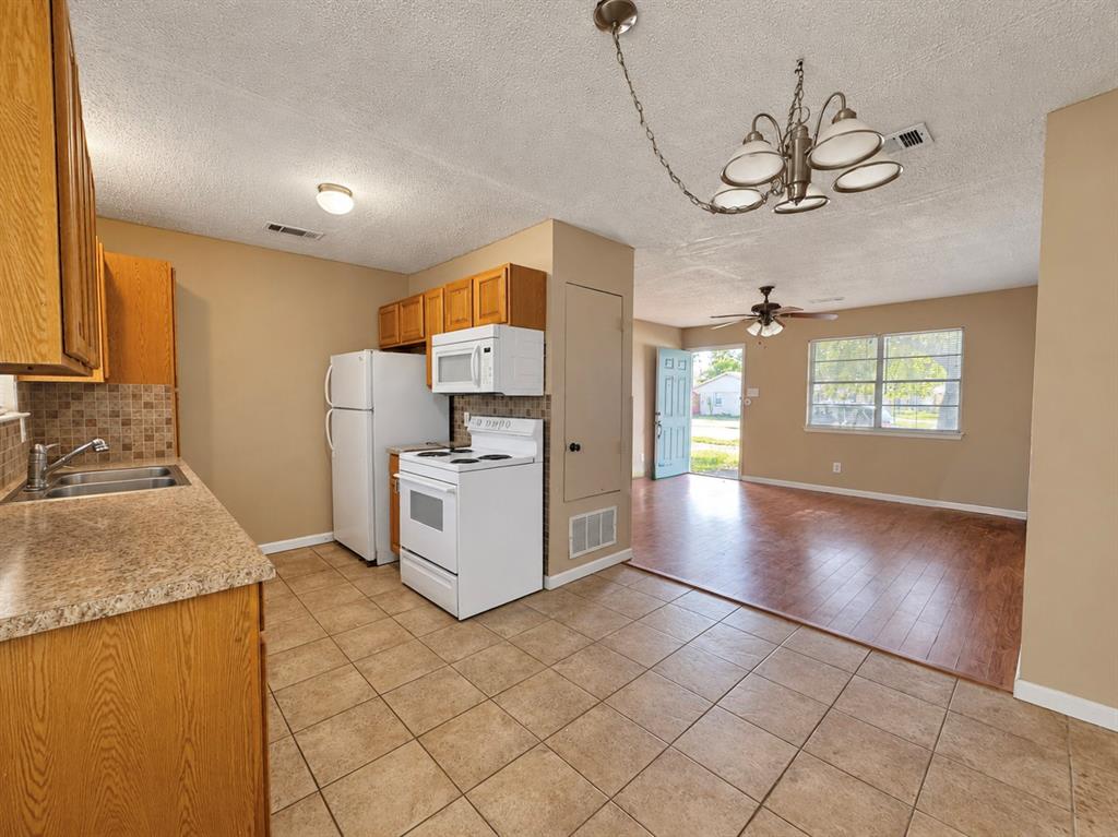 Kitchen featuring cabinetry with light wood finish, tile flooring, stone-finish countertops, mosaic tile backsplash, and a multi-arm hanging chandelier
