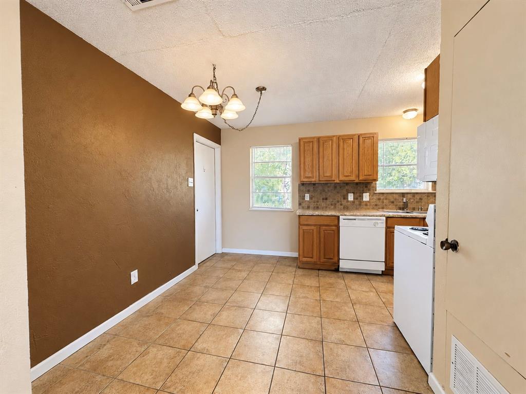 Kitchen featuring wood cabinetry, stone-finish tile backsplash, tile flooring, and a multi-arm chandelier