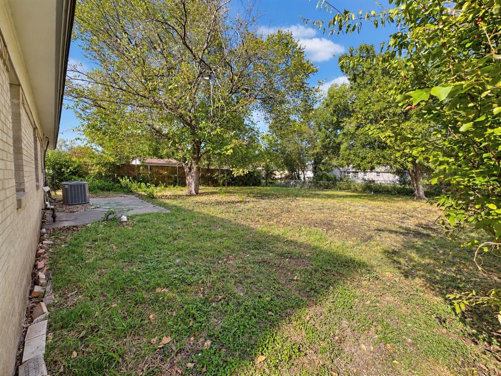 Backyard featuring a concrete patio, light-toned brick exterior, mature trees, and perimeter fencing