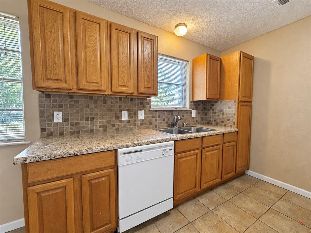 Kitchen featuring wood cabinetry, stone-patterned laminate countertops, a mosaic tile backsplash, a double-basin stainless steel sink, and ceramic tile flooring