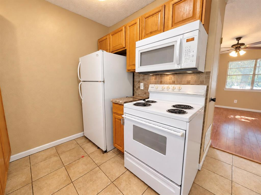 Kitchen featuring natural wood cabinetry, white appliances, a tiled backsplash, and ceramic tile flooring