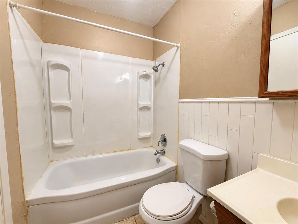Bathroom featuring a tub-shower combination with integrated shelving, vertical wainscoting, and a vanity with a molded sink
