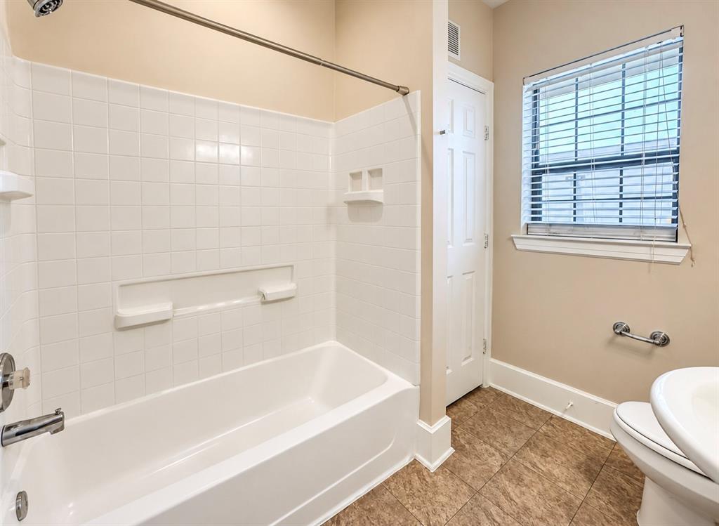 Bathroom featuring a white tile tub surround with integrated shelving, metallic fixtures, a window with horizontal blinds, and tile flooring