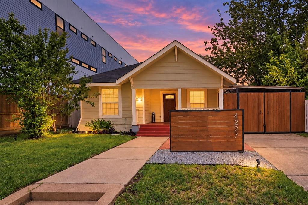 Exterior facade featuring horizontal siding, a covered front porch, a custom wood-slat privacy screen, a concrete driveway, and an attached storage structure