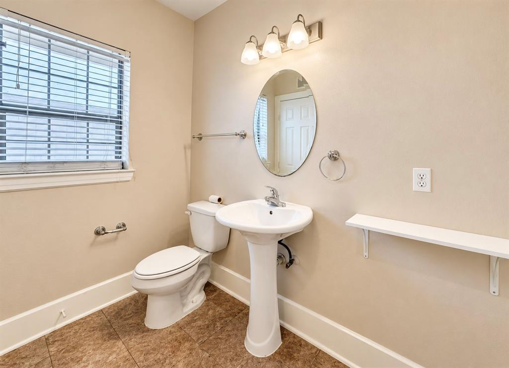 Bathroom featuring tile flooring, a porcelain pedestal sink with a chrome faucet, an oval wall-mounted mirror, three-light vanity fixture, and a built-in wall shelf