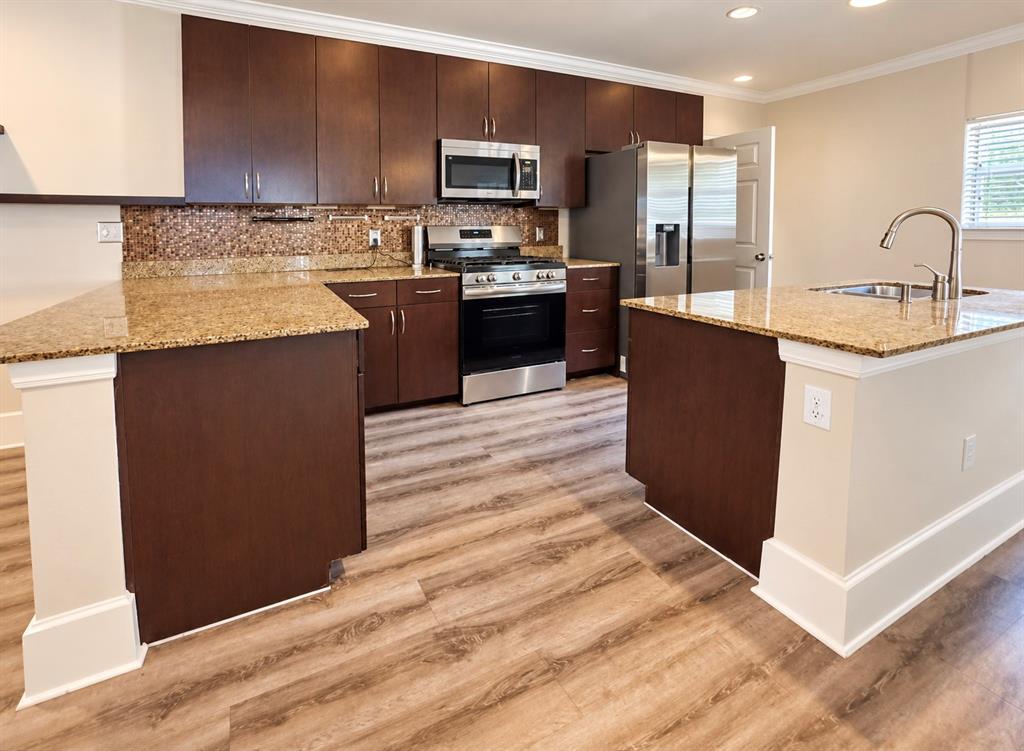 Kitchen featuring dark-finish cabinetry, stone-surface countertops, stainless steel appliances, a mosaic tile backsplash, and wood-finish flooring