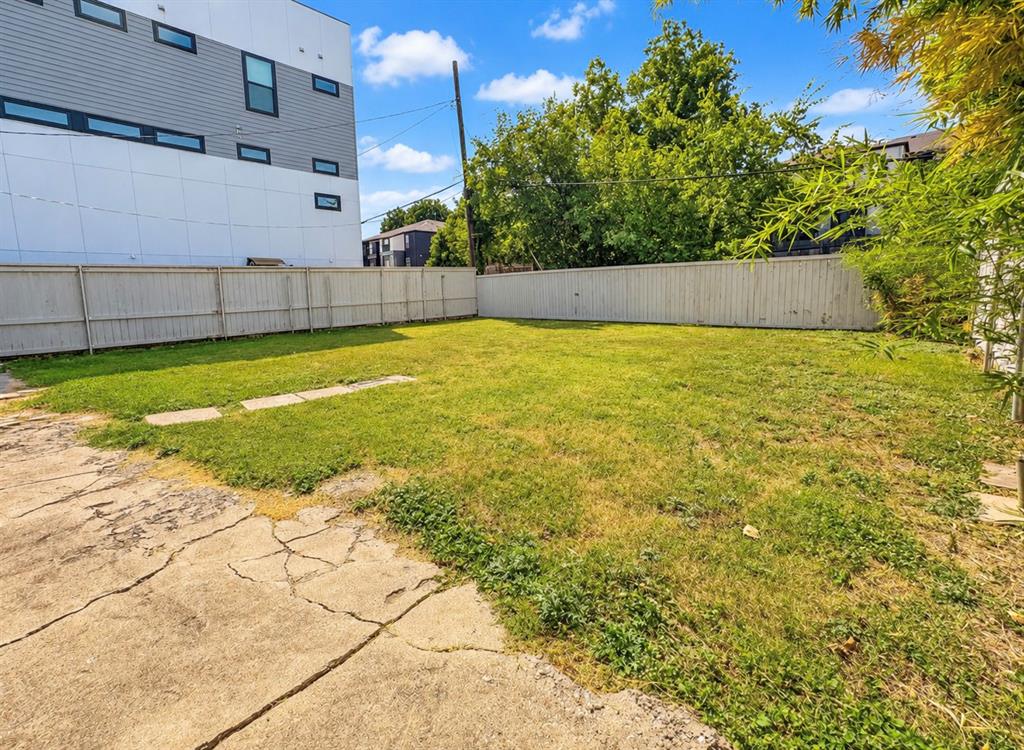 Fenced backyard featuring a grass lawn, concrete hardscaping, and mature trees