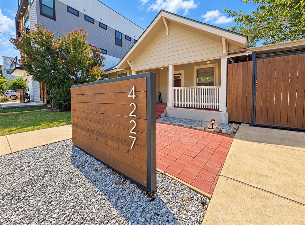 Exterior facade featuring a covered front porch with white railing, horizontal wood-plank privacy screening, a paver patio, and low-maintenance gravel landscaping
