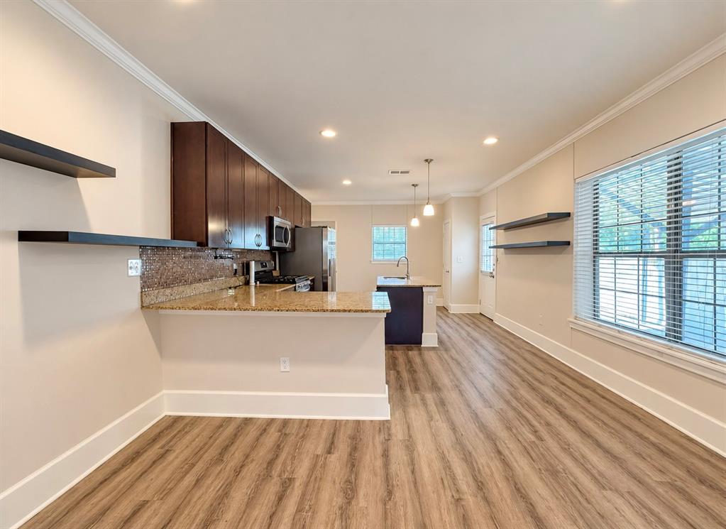Kitchen featuring wood-finish flooring, dark wood cabinetry, stone countertops, mosaic tile backsplash, and floating wall shelves