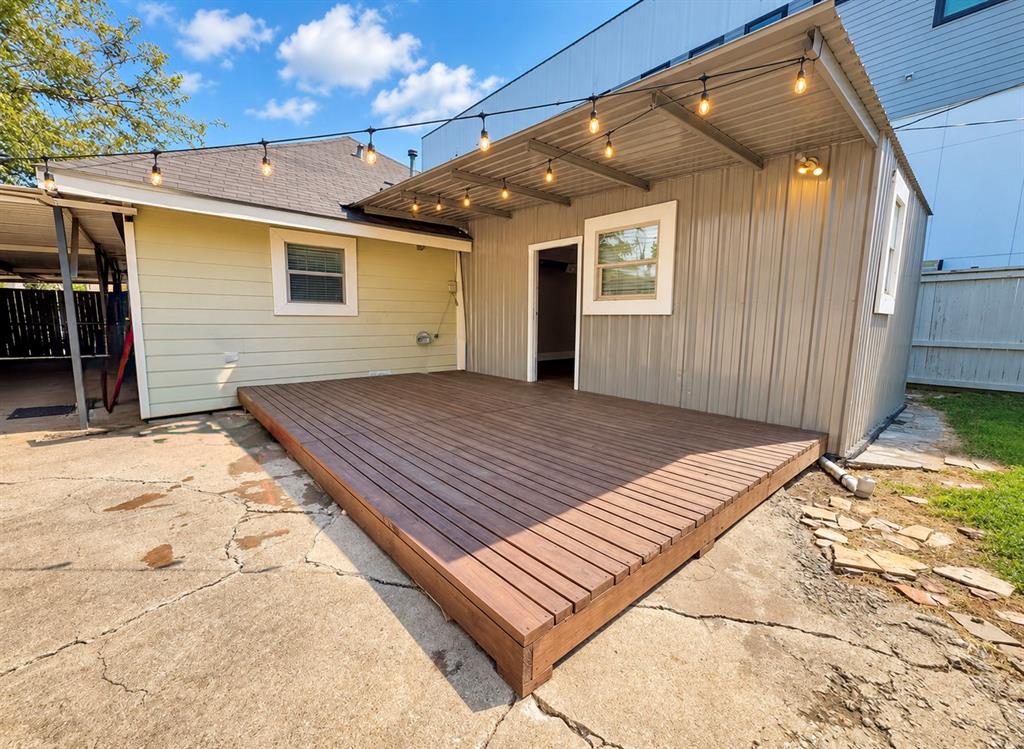 Wood-finish platform deck with an attached corrugated metal awning, overhead string lighting, and exterior lap siding