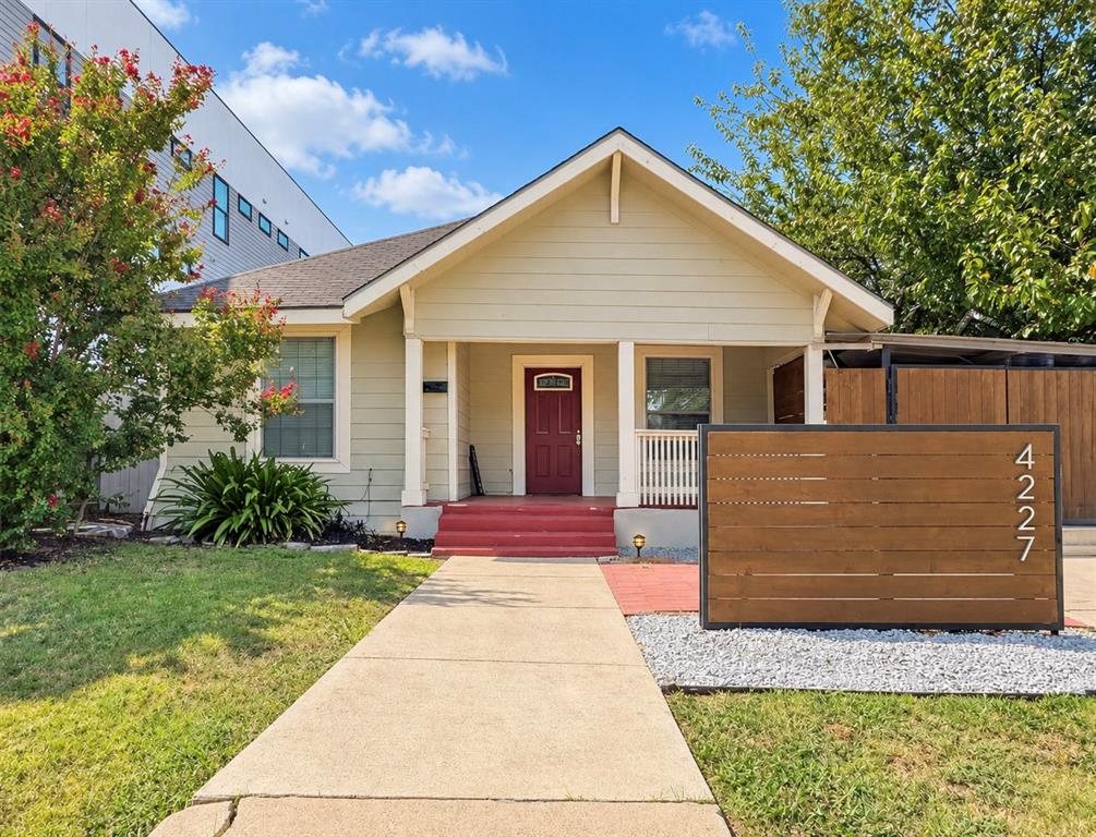 Single-story exterior featuring horizontal siding, a covered front porch with squared columns, a solid wood-finish slat privacy screen, and a concrete walkway