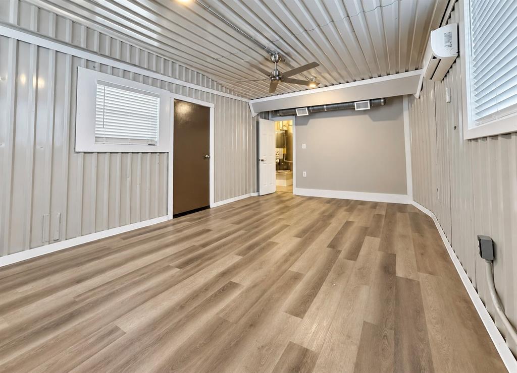 Interior space featuring corrugated metal walls and ceiling, wood-finish flooring, a ceiling fan, and a wall-mounted mini-split system