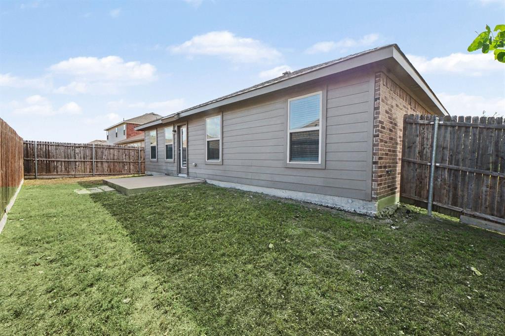 Exterior rear elevation featuring horizontal siding, brick masonry, a concrete patio, and a wood privacy fence enclosing the lawn