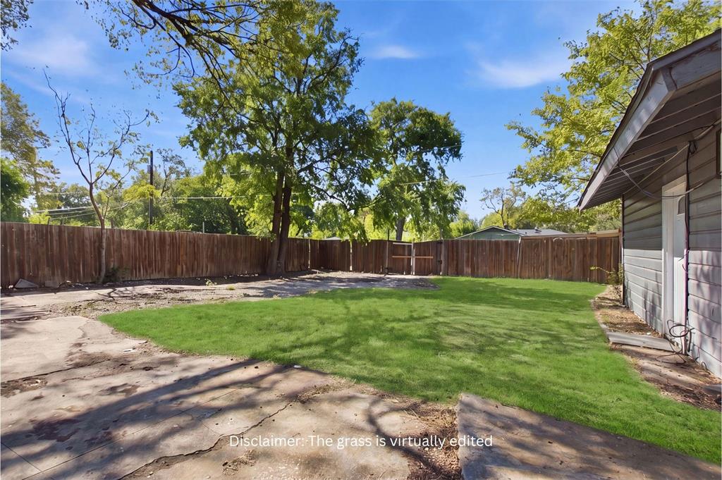 Backyard featuring a grass lawn, expansive concrete patio, horizontal wood fencing, and mature trees