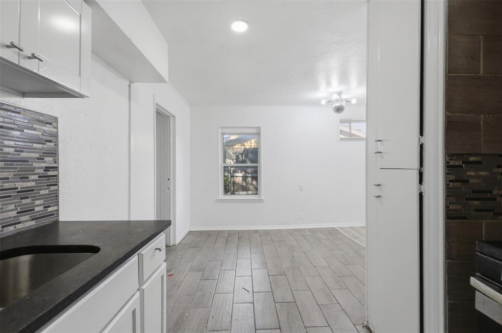 White cabinetry, dark countertops, wood-finish tile flooring, mosaic tile backsplash, and recessed ceiling lighting White cabinetry, dark countertops, wood-finish tile flooring, mosaic tile backsplash, and recessed ceiling lighting