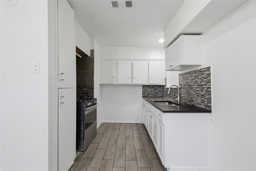 Kitchen featuring white cabinetry, wood-finish flooring, dark countertops, a stainless steel gas range, and a decorative tile backsplash Kitchen featuring white cabinetry, wood-finish flooring, dark countertops, a stainless steel gas range, and a decorative tile backsplash