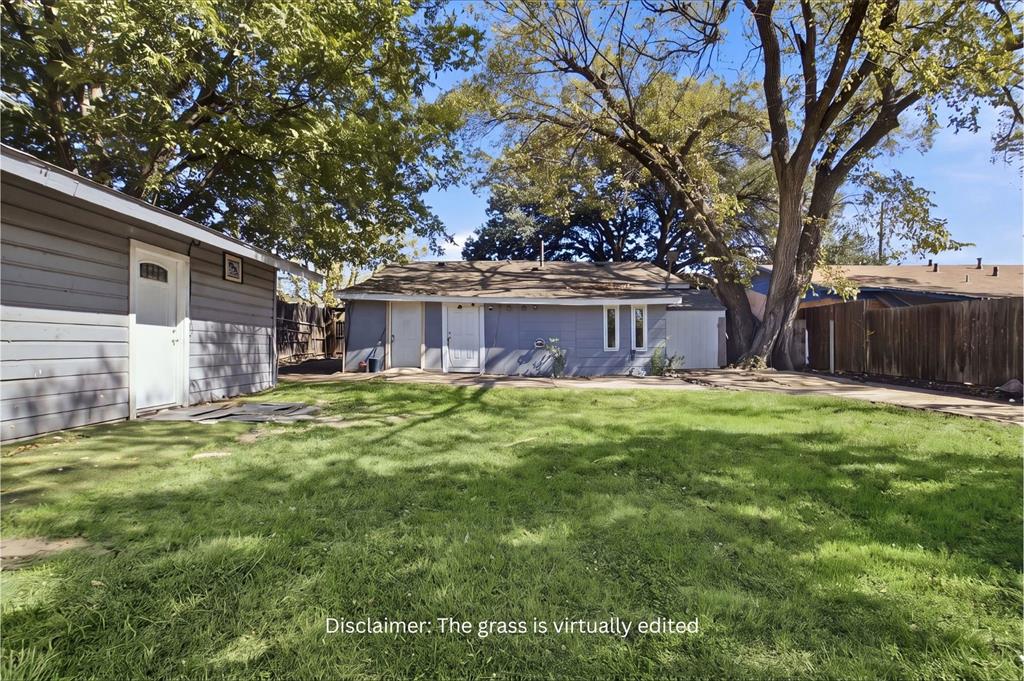 Expansive backyard featuring a large grass area, mature trees, wood privacy fencing, and a detached outbuilding with horizontal siding