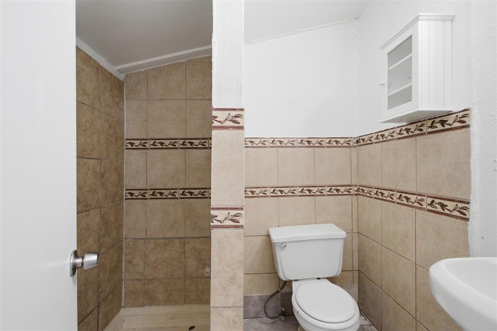 Full-height ceramic wall tiling featuring a decorative border, wall-mounted storage cabinet, and white porcelain toilet