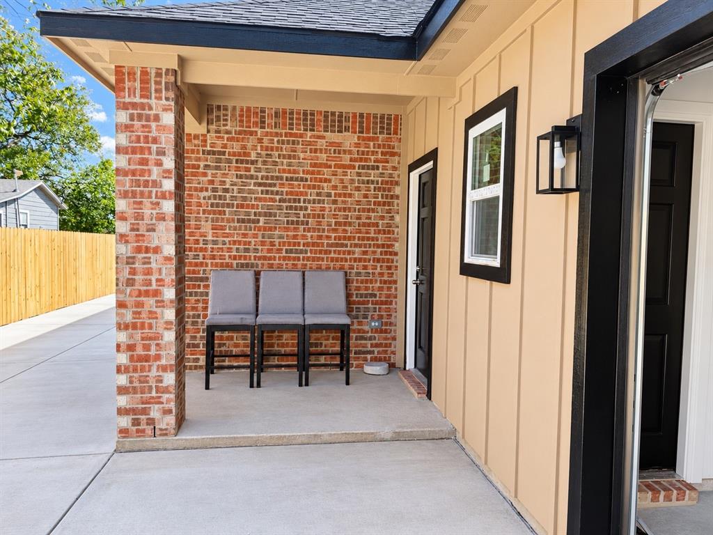 Covered patio featuring a red brick accent wall, vertical wood-finish siding, concrete flooring, and a contemporary black exterior wall-mounted light fixture