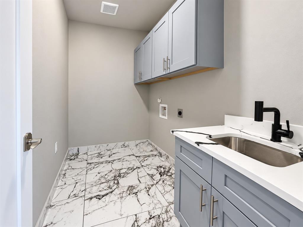 Utility area featuring marble-patterned tile flooring, gray Shaker-style cabinetry, white solid-surface countertops with an integrated stainless steel sink, and matte black plumbing fixtures