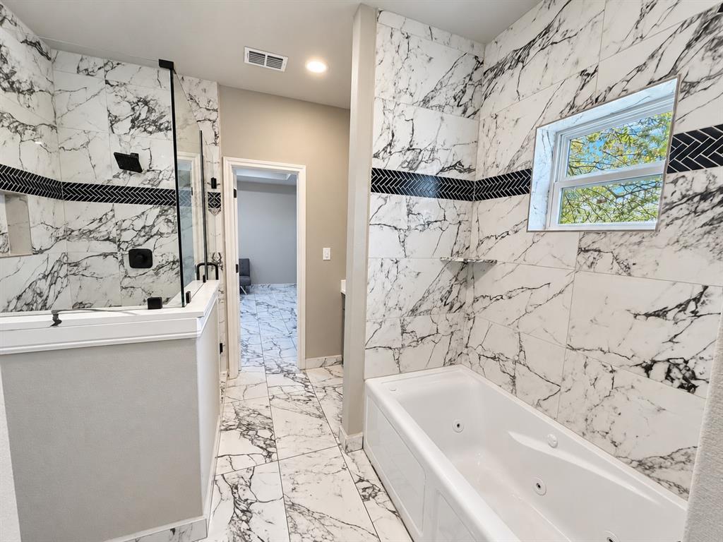Bathroom featuring large-format veined tile surround, a built-in jetted soaking tub, a walk-in glass-enclosed shower with matte black fixtures, and a decorative herringbone-patterned accent border