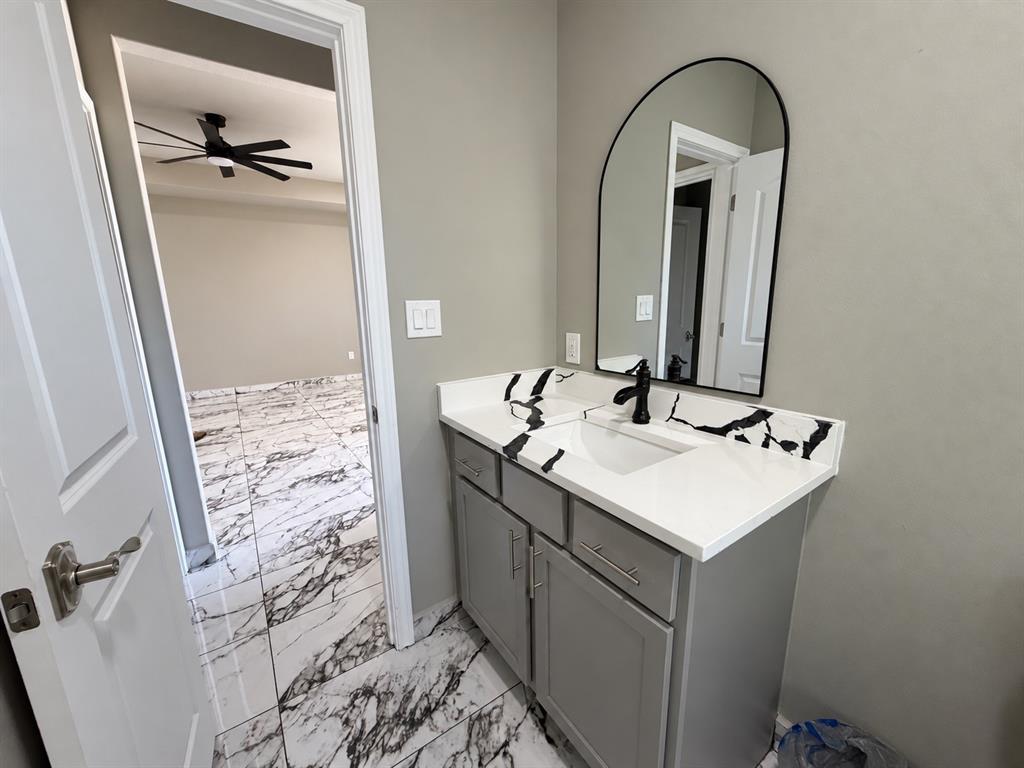 Bathroom vanity featuring gray cabinetry, a white countertop with black veining, an integrated rectangular sink, a matte black faucet, and an arched wall-mounted mirror