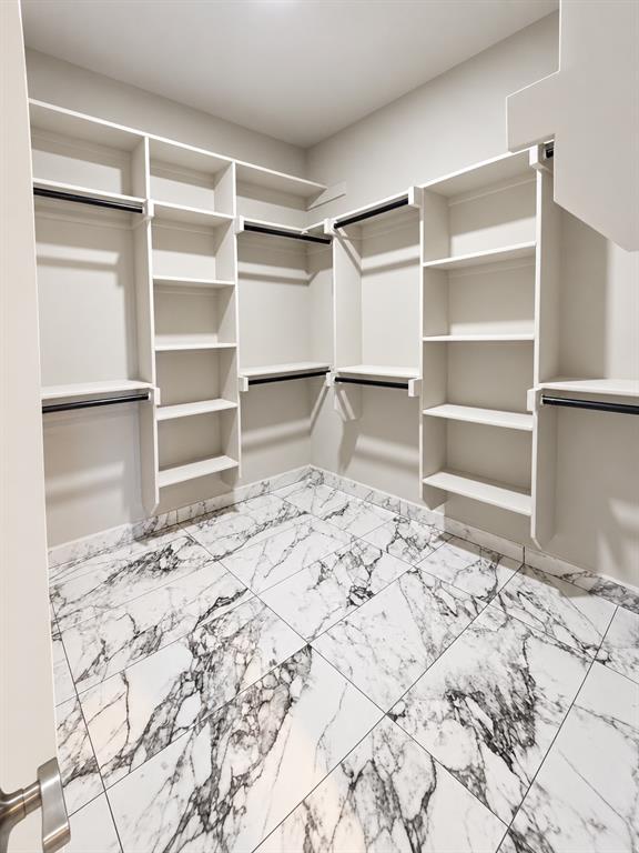 Walk-in closet featuring extensive built-in white shelving, integrated hanging rods, and large-format porcelain tile flooring with a veined pattern