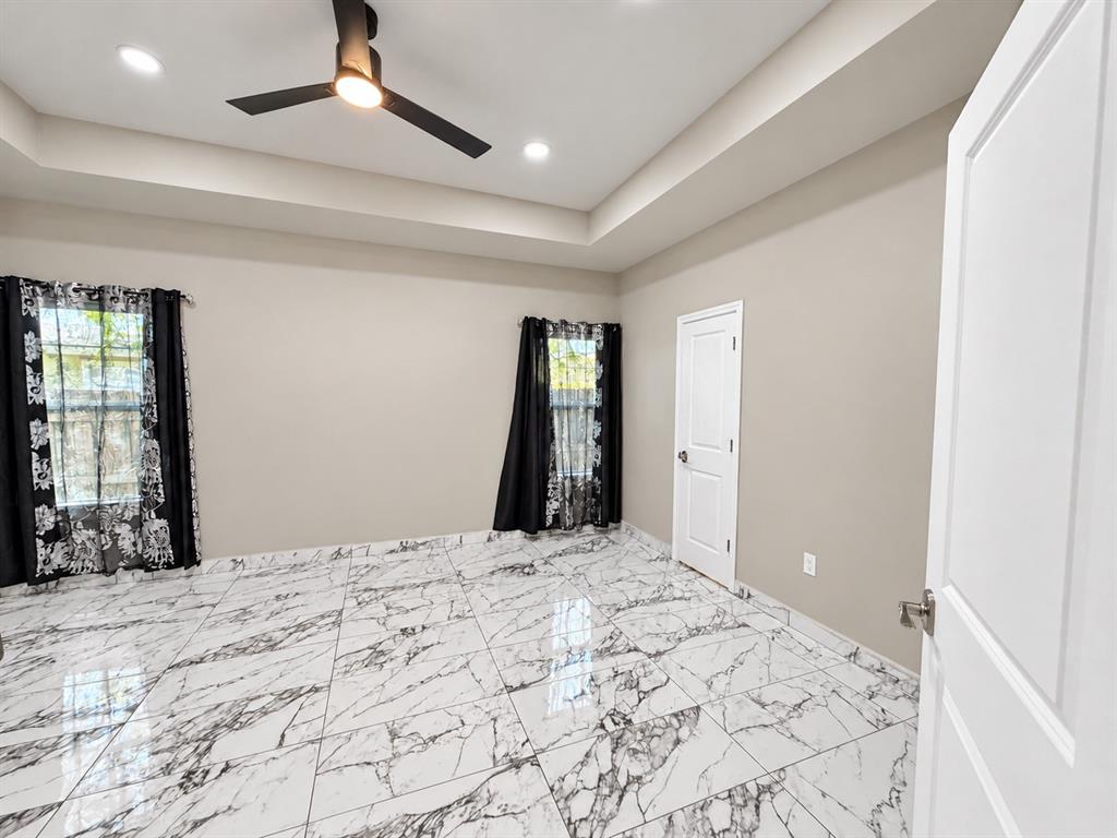 Tray ceiling featuring recessed lighting and a matte black ceiling fan, complemented by large-format high-gloss patterned tile flooring