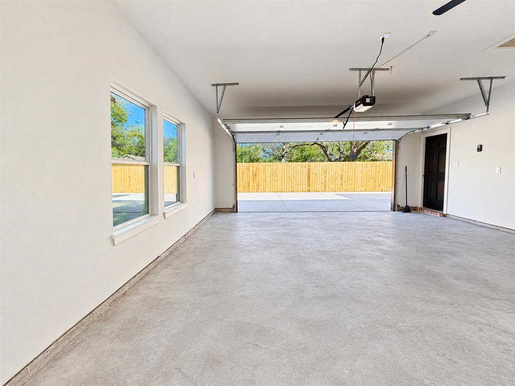 Spacious multi-car garage featuring smooth-finished concrete flooring, dual-pane windows, a dark-finish entry door, and an automatic overhead door opener