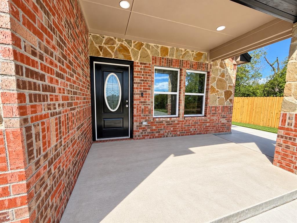 Covered entryway featuring a brick and stone facade, concrete porch, and a front door with an oval glass insert Covered entryway featuring a brick and stone facade, concrete porch, and a front door with an oval glass insert