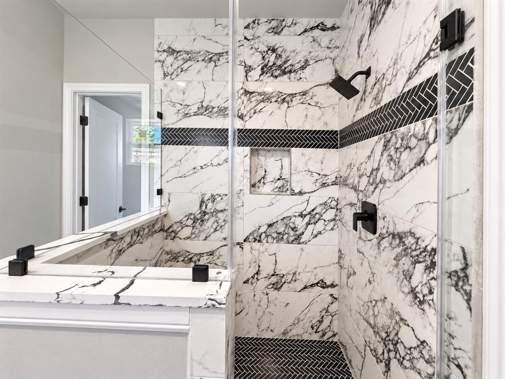 Walk-in shower featuring floor-to-ceiling large-format veined tile, integrated wall niche, matte black fixtures, and a decorative herringbone tile accent border