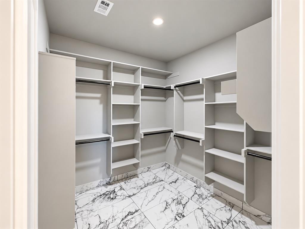 Walk-in closet featuring floor-to-ceiling white built-in shelving, multiple hanging rods, and stone-finish tile flooring