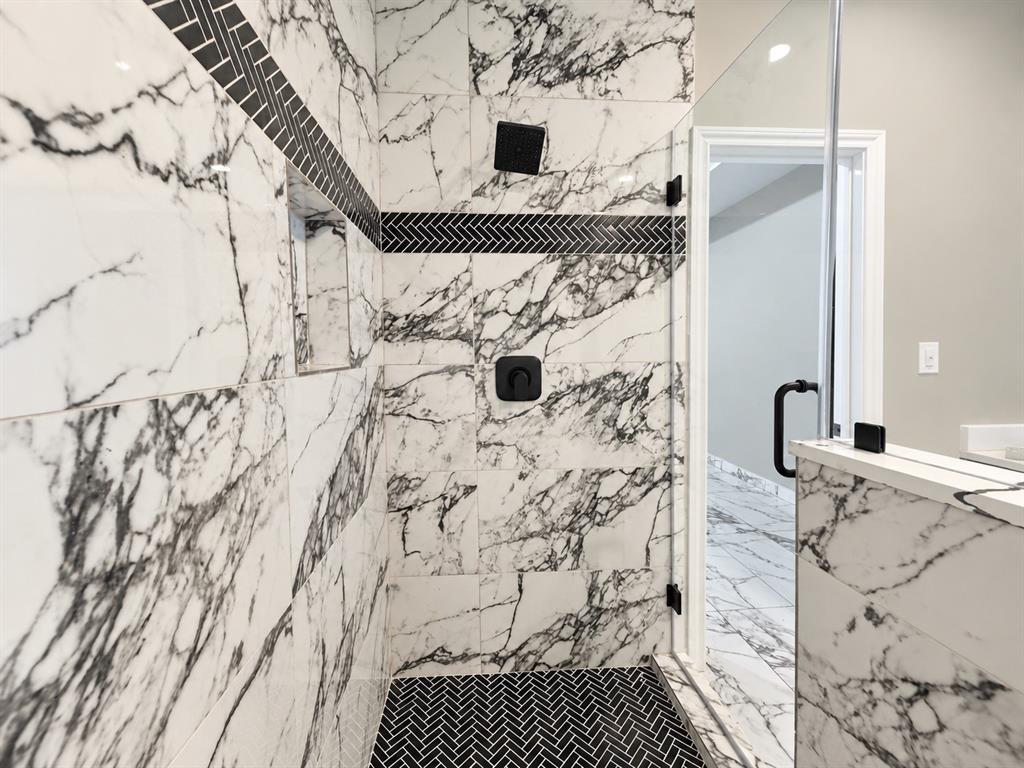 Walk-in shower featuring large-format patterned wall tile, a herringbone tile floor, a built-in recessed niche, a rainfall showerhead, and a frameless glass enclosure