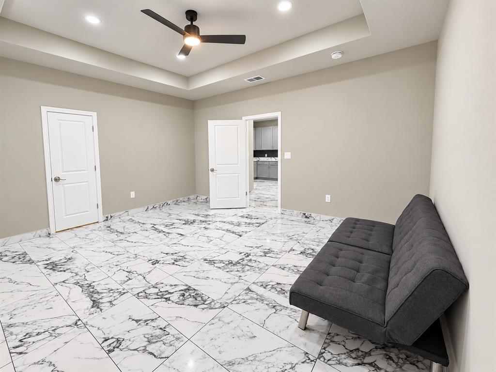 Tray ceiling featuring recessed lighting, large-format stone-patterned tile flooring, and a matte black ceiling fan with integrated light