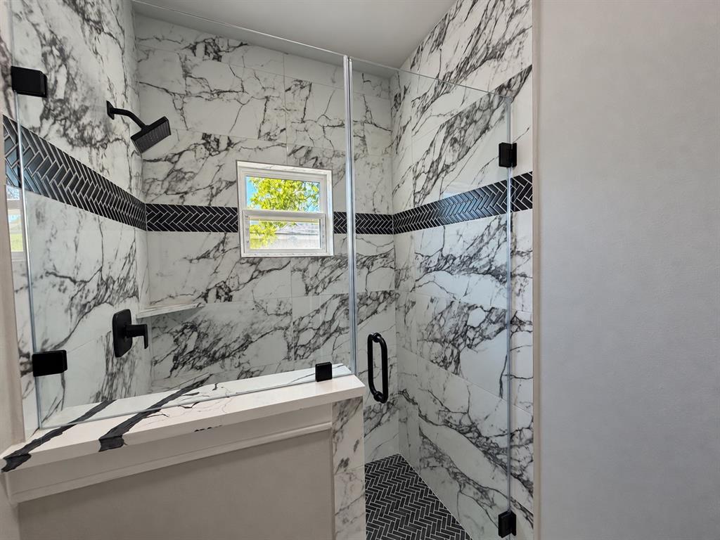 Walk-in shower featuring large-format patterned wall tile, a contrasting herringbone accent border, a glass enclosure, a built-in stone-top ledge, and matte black plumbing fixtures