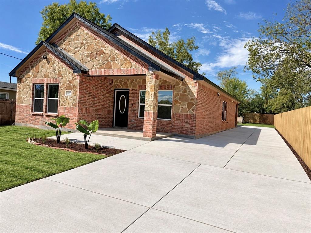 Single-story exterior featuring a brick and stone facade, covered front entryway, expansive concrete driveway, and wooden privacy fencing Single-story exterior featuring a brick and stone facade, covered front entryway, expansive concrete driveway, and wooden privacy fencing