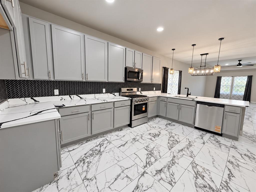 Kitchen featuring light gray shaker cabinetry, quartz countertops with veining, a black herringbone tile backsplash, stainless steel appliances, and large-format patterned tile flooring