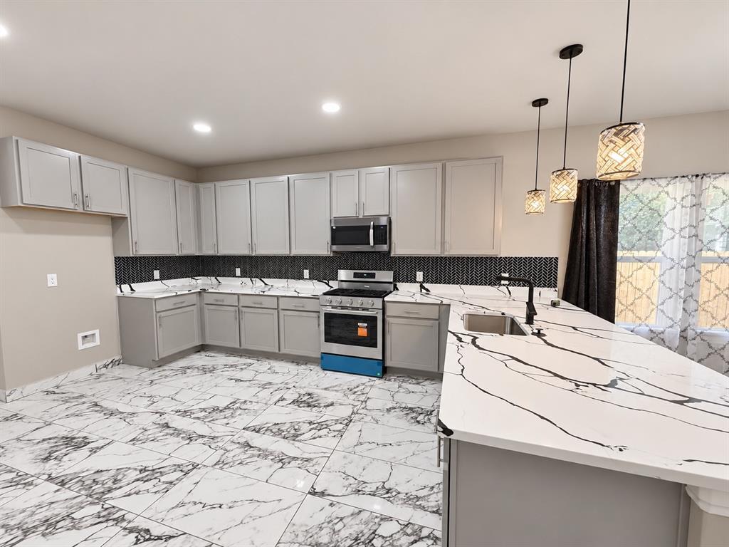 Kitchen featuring light gray cabinetry, large-format veined tile flooring, solid surface countertops with contrasting veining, a decorative geometric tile backsplash, and three suspended pendant lights